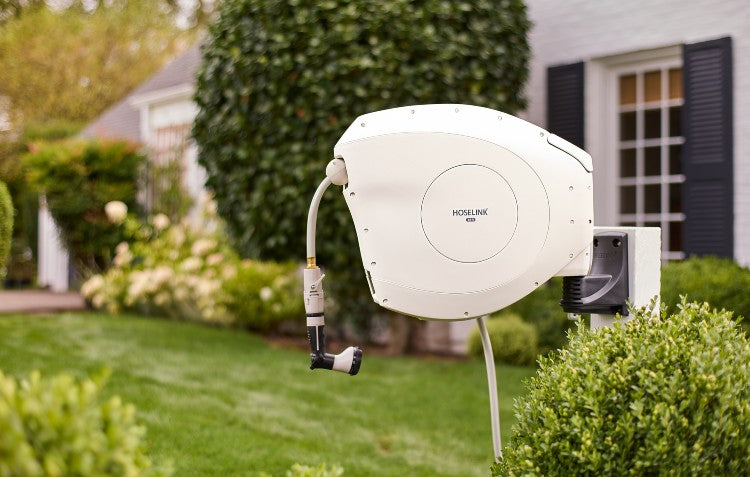 Image of Hoselink Beige Retractable Hose Reel in a garden setting with a white house in the background
