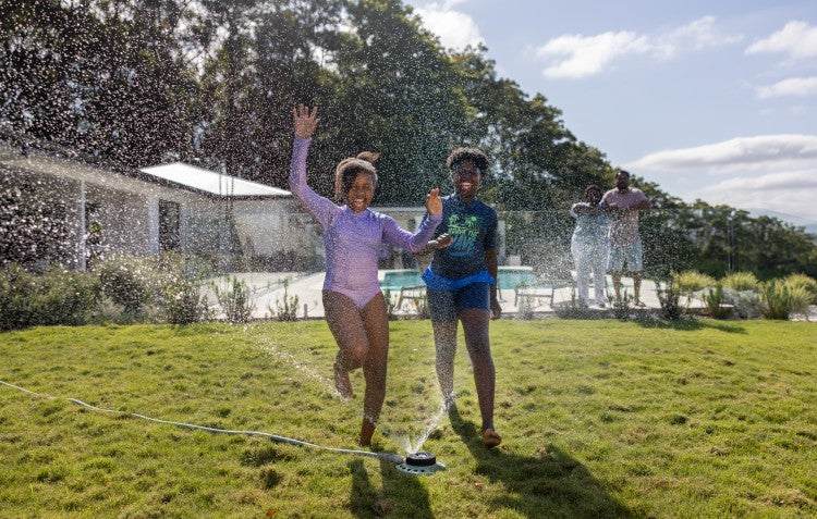 kids running through sprinkler on lawn