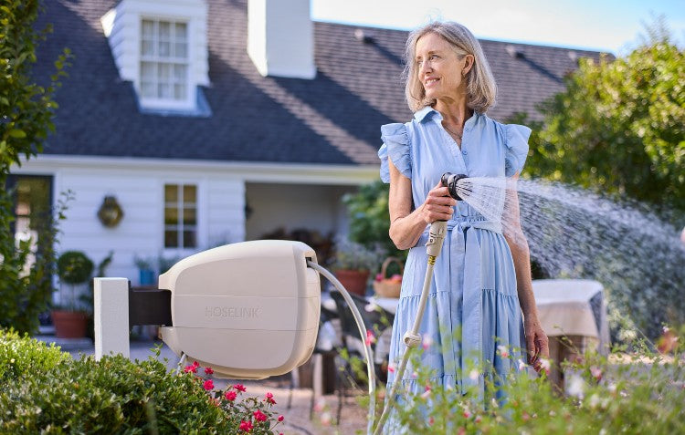 Image of woman watering her flower garden with a beige colored Evolve Hose Reel