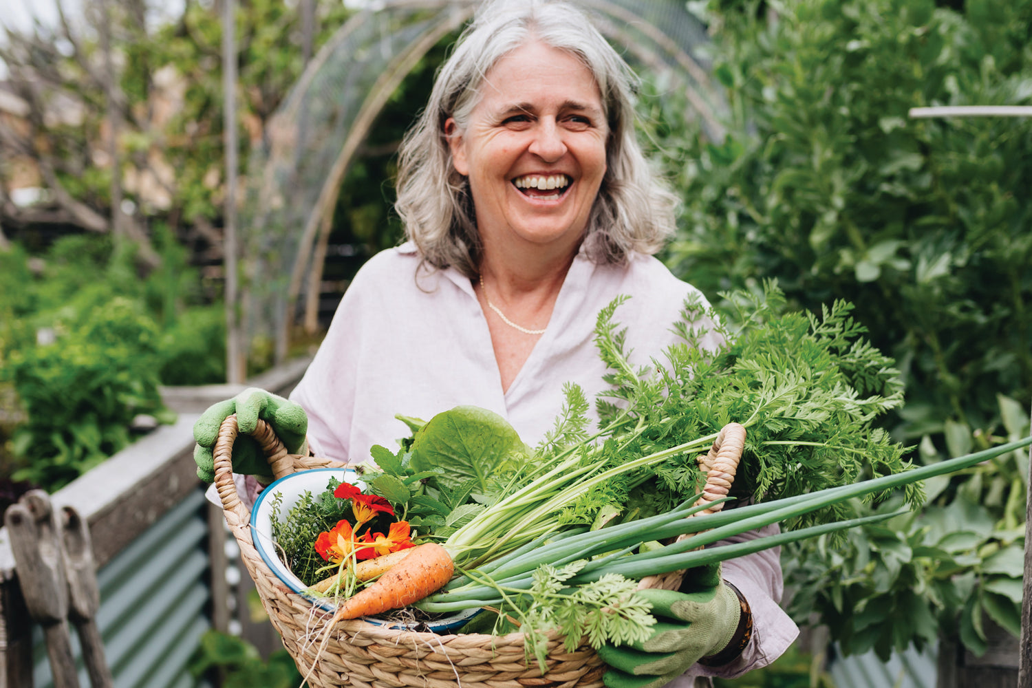 Female in garden carrying basket of vegetables while smiling