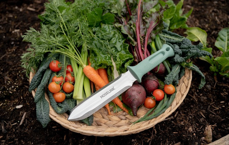 stainless steel hori hori garden knife sitting on top of a basket of vegetables