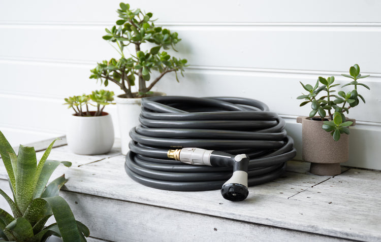 Image of dark hose coiled with sprayer attached set on cement ledge