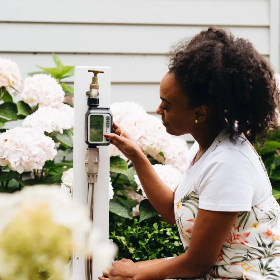Woman using a Hoselink automatic hose timer with rain sensor on an outdoor faucet in a garden