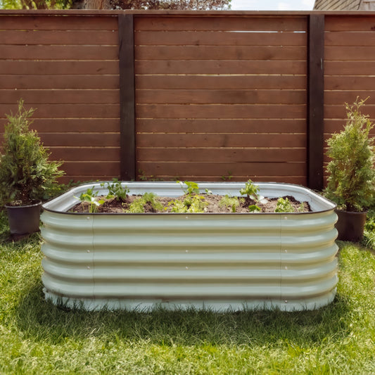 6 in 1 Garden Bed in front of a brown fence behind. Garden bed is full of plants and earth.