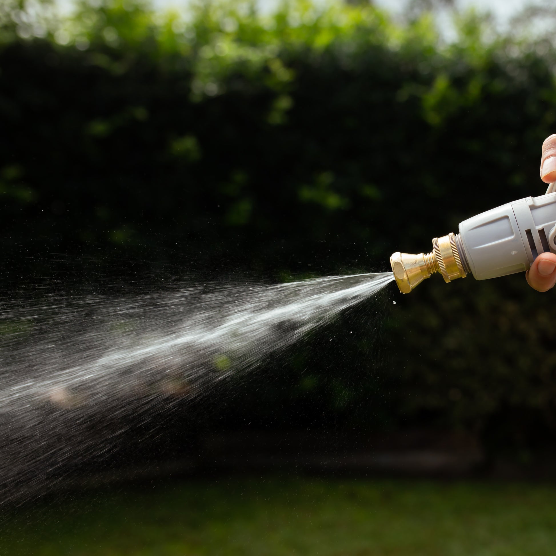 Hand holding a brass high pressure jet nozzle with water spurting out of it