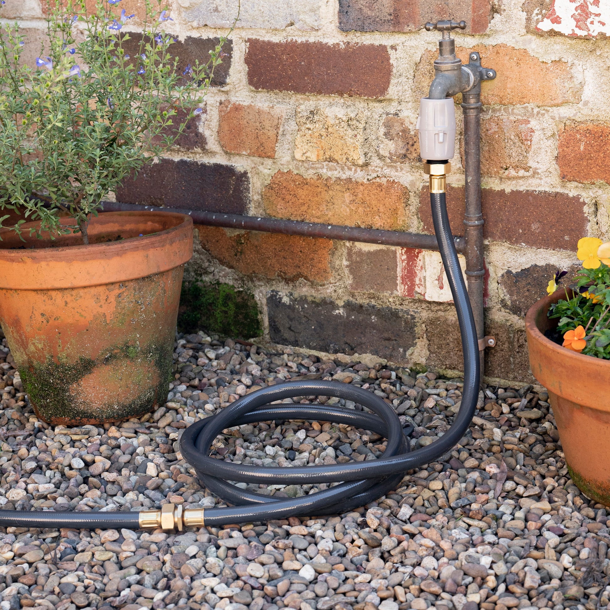 Charcoal Leader Hose coiled on the ground connected to the faucet at one end and a garden hose at the other end