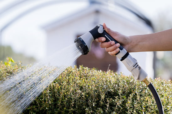 Female hand holding Comfort 8-Pattern Spray Nozzle and using it to water garden