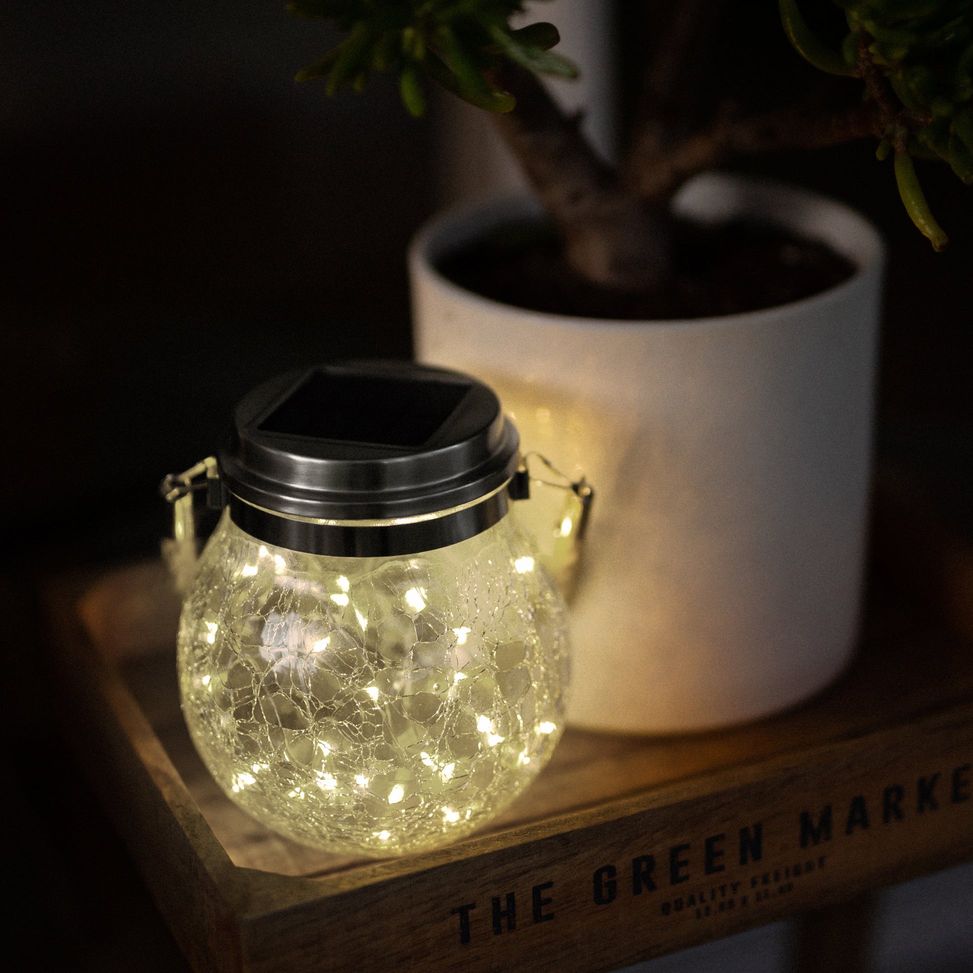 Solar crackle jar light turned on and sitting on a wooden tray next to a plant