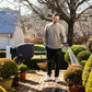 Man watering plants in a garden with an evolve hose reel with charcoal cover, surrounded by potted plants and a house in the background.
