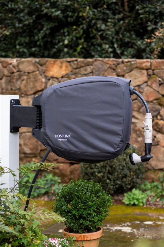 hoselink evolve reel with charcoal cover mounted on a white post with plants and stone wall in the background.