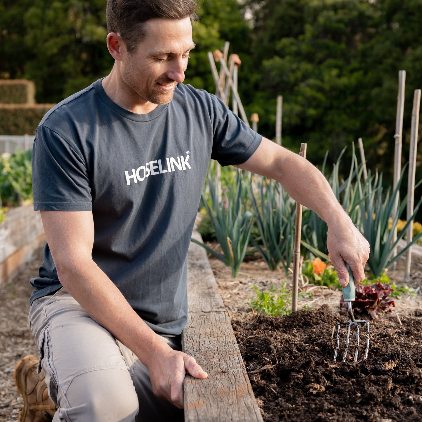 Man using Garden Fork tool in a raised bed with 'HOSELINK' t-shirt