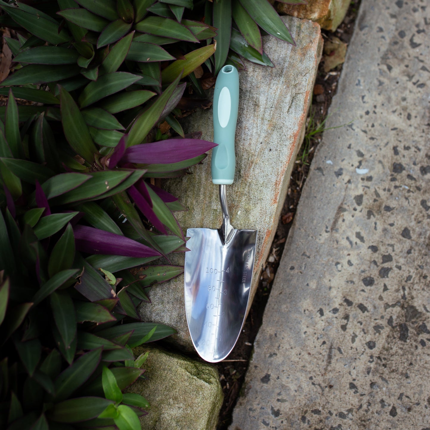 Garden Trowel on a stone surface with plants in the background
