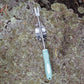 Garden weeder with a sage green handle on a textured surface