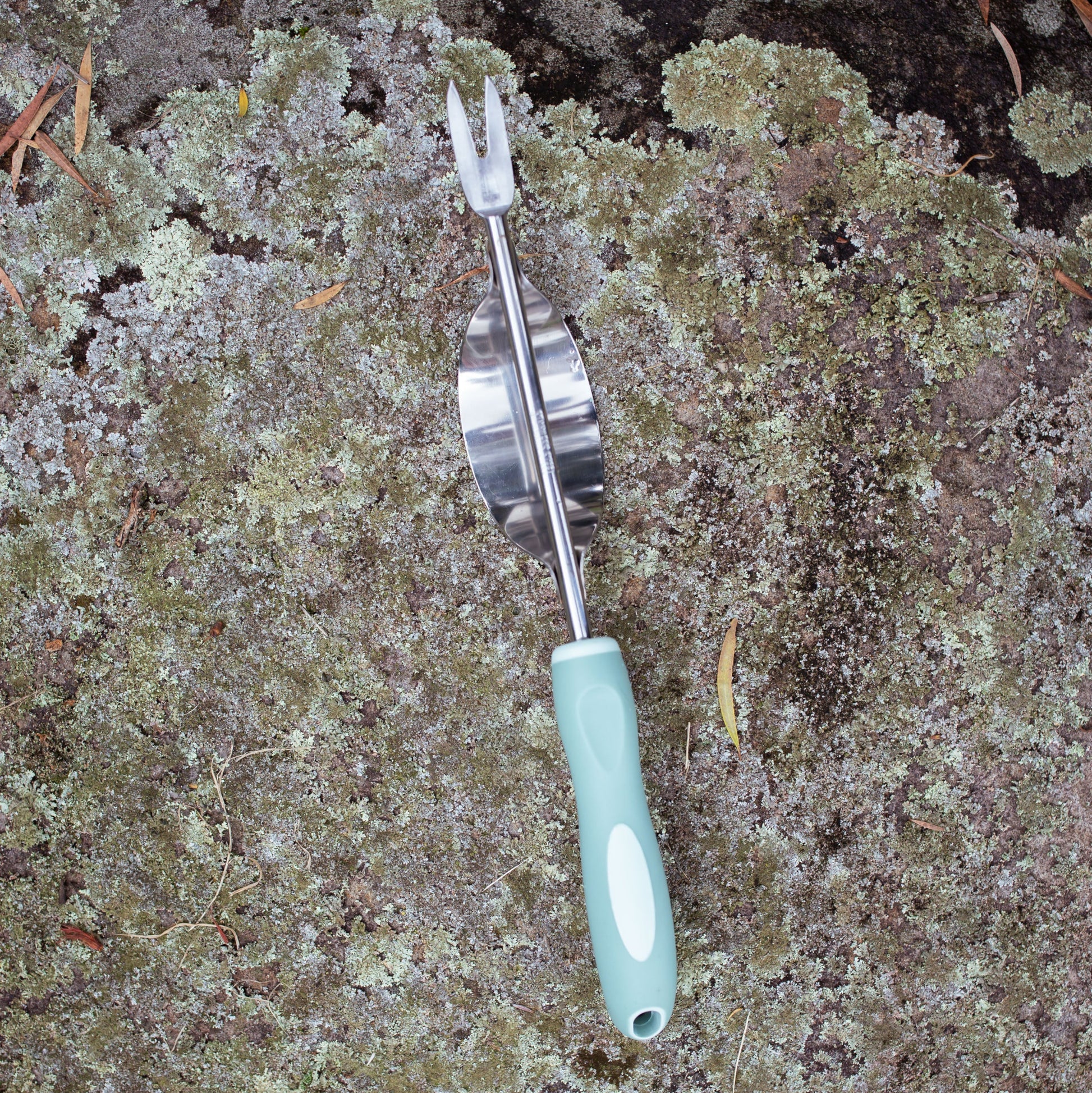 Garden weeder with a sage green handle on a textured surface