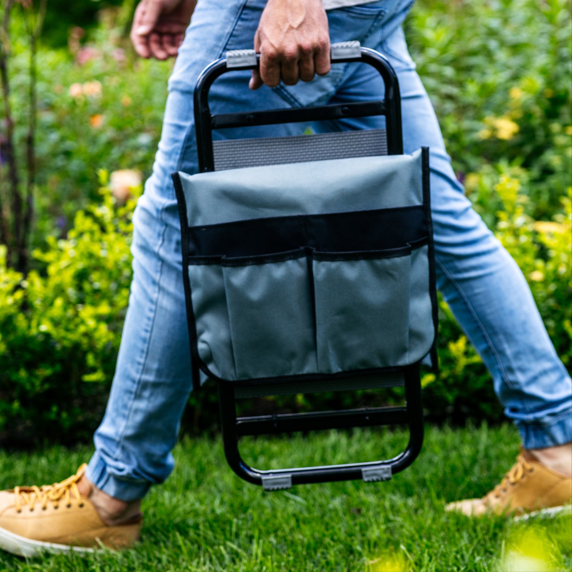 Person walking with folded up garden kneeler and seat across lawn with garden in background