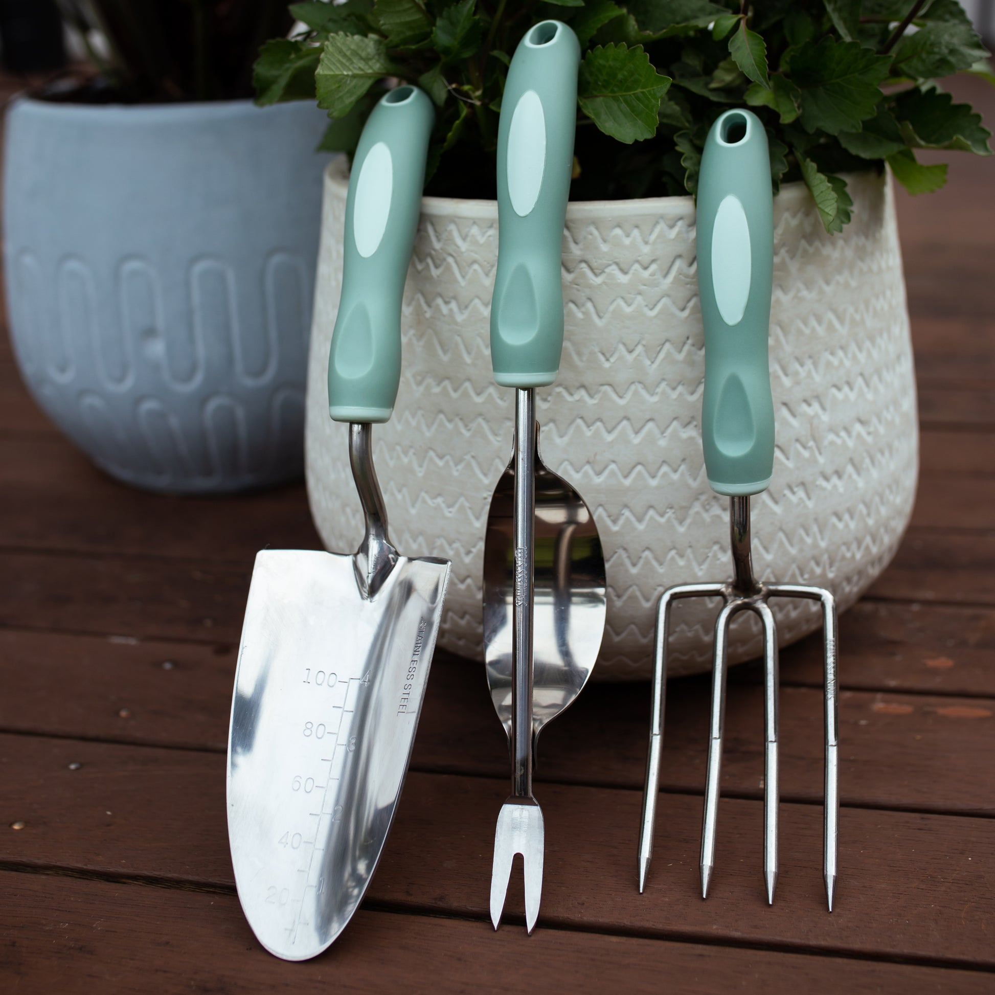 Gardening tools set with green handles on a wooden surface.