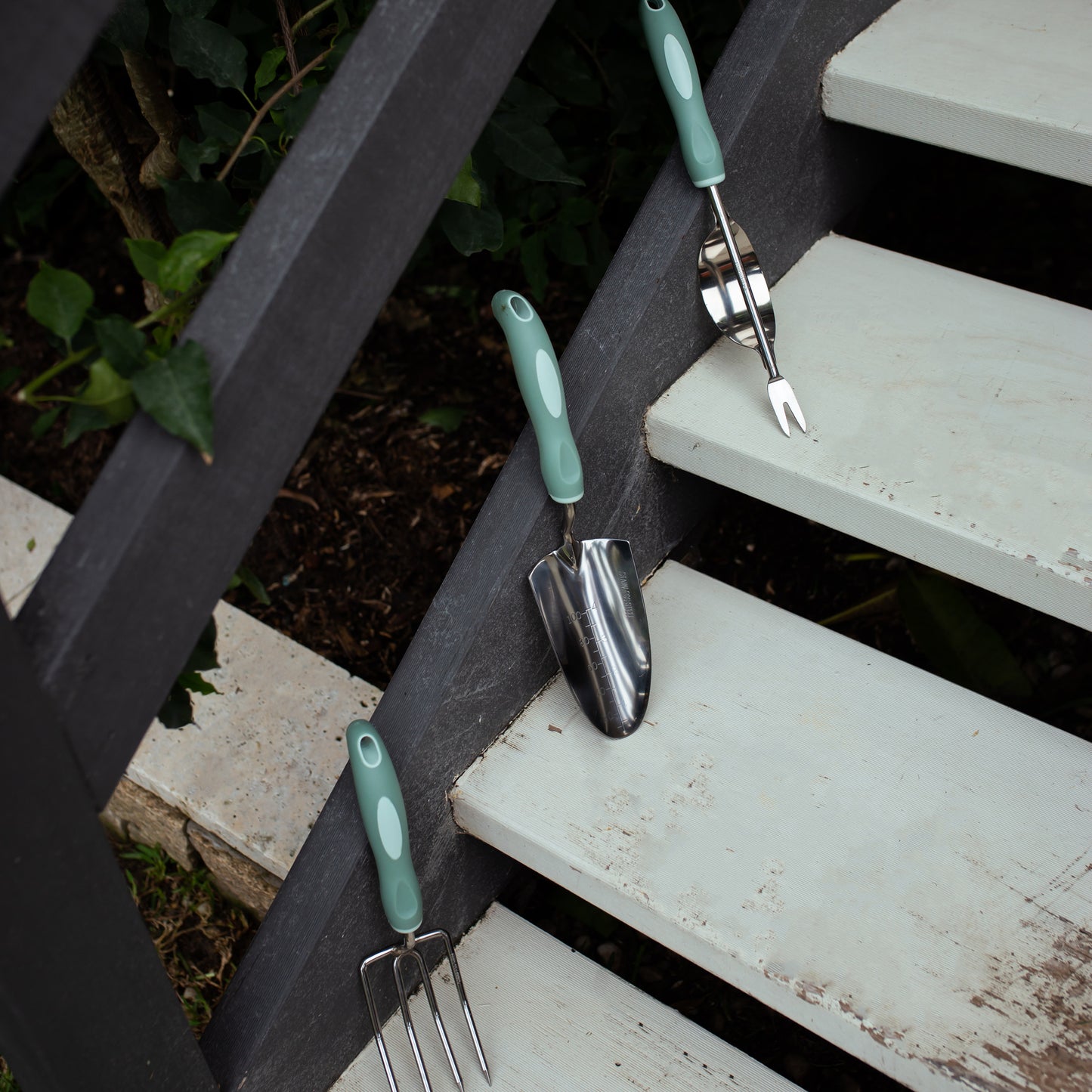 Gardening tools with green handles on a set of outdoor stairs.