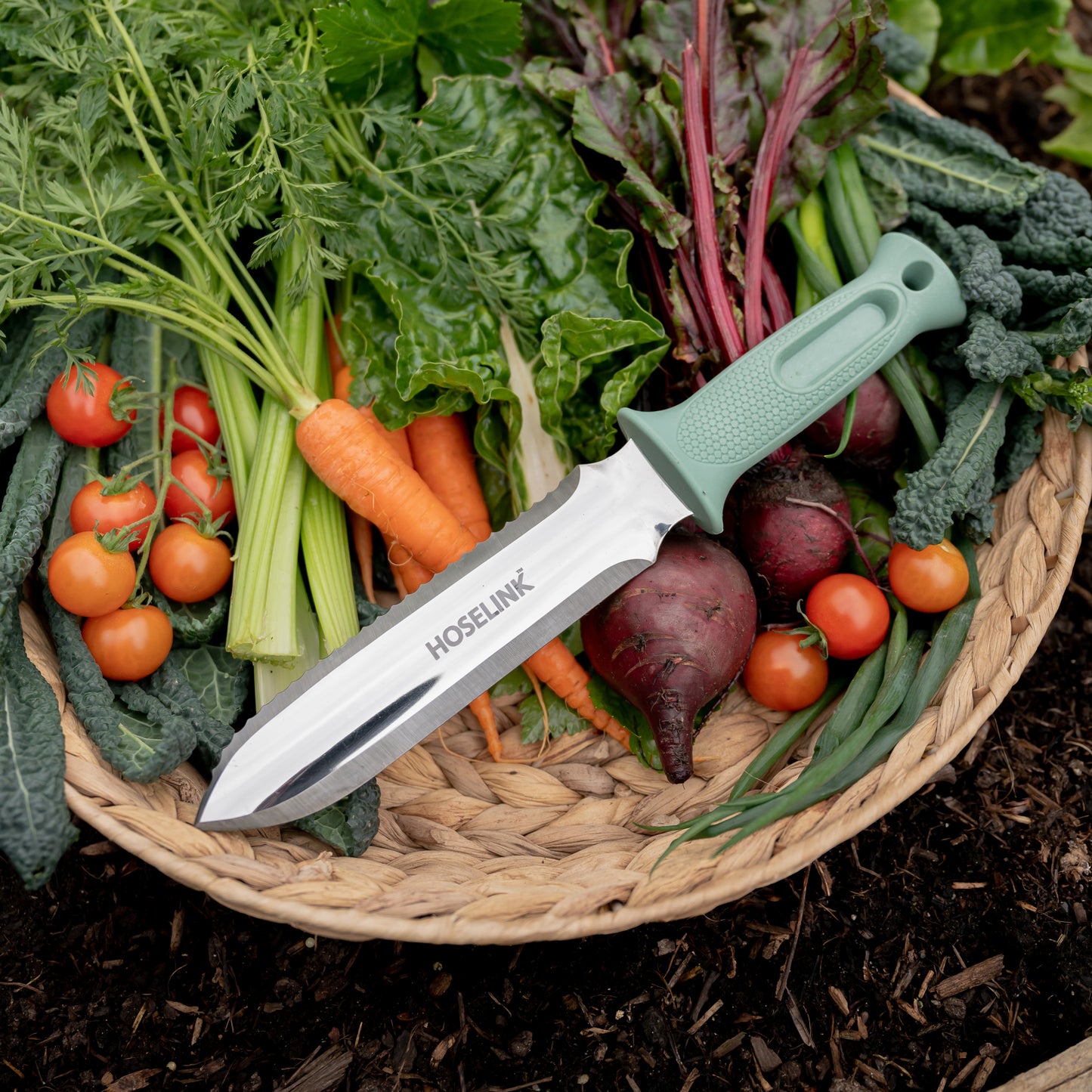 green garden knife lying in a basket on top of fresh garden vegetables 