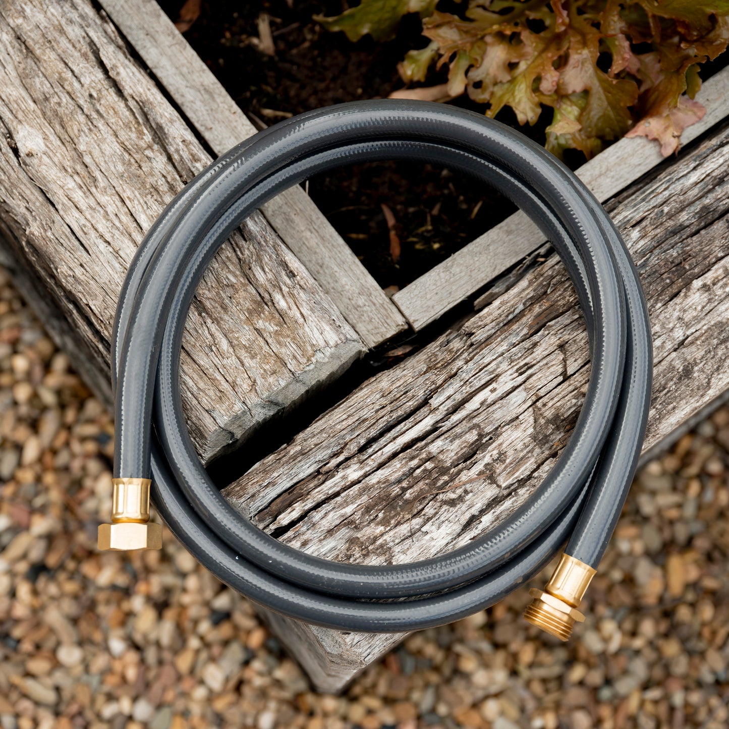 Coiled dark grey leader hose on edge of raised garden bed