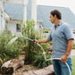 Man watering garden beds on front porch with a garden hose and spray wand