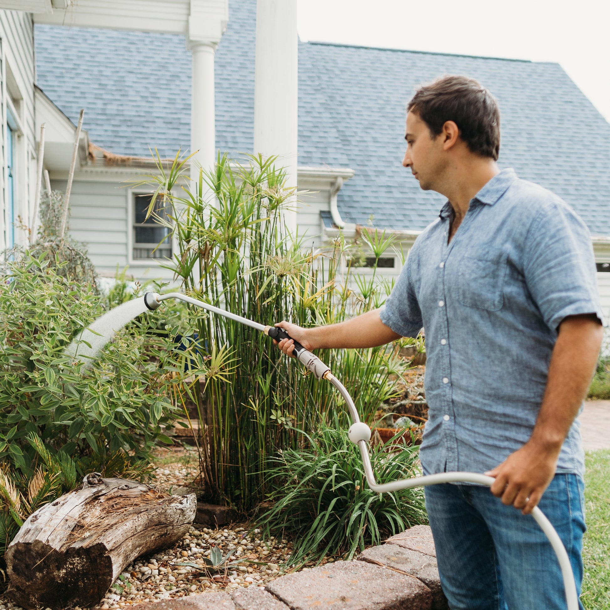 Man watering garden beds on front porch with a garden hose and spray wand