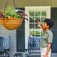 Woman watering a hanging basket of flowers on a porch