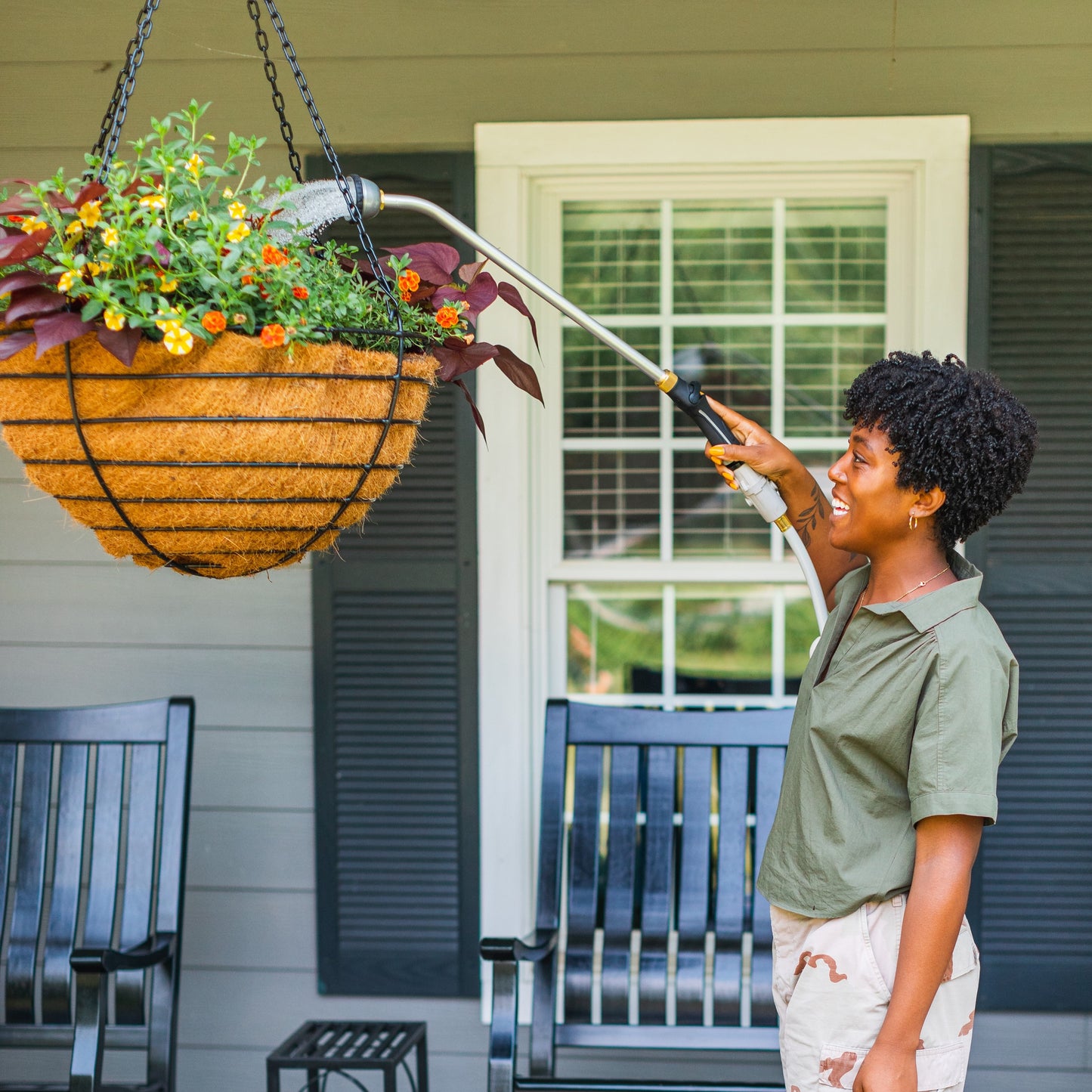 Woman watering a hanging basket of flowers on a porch