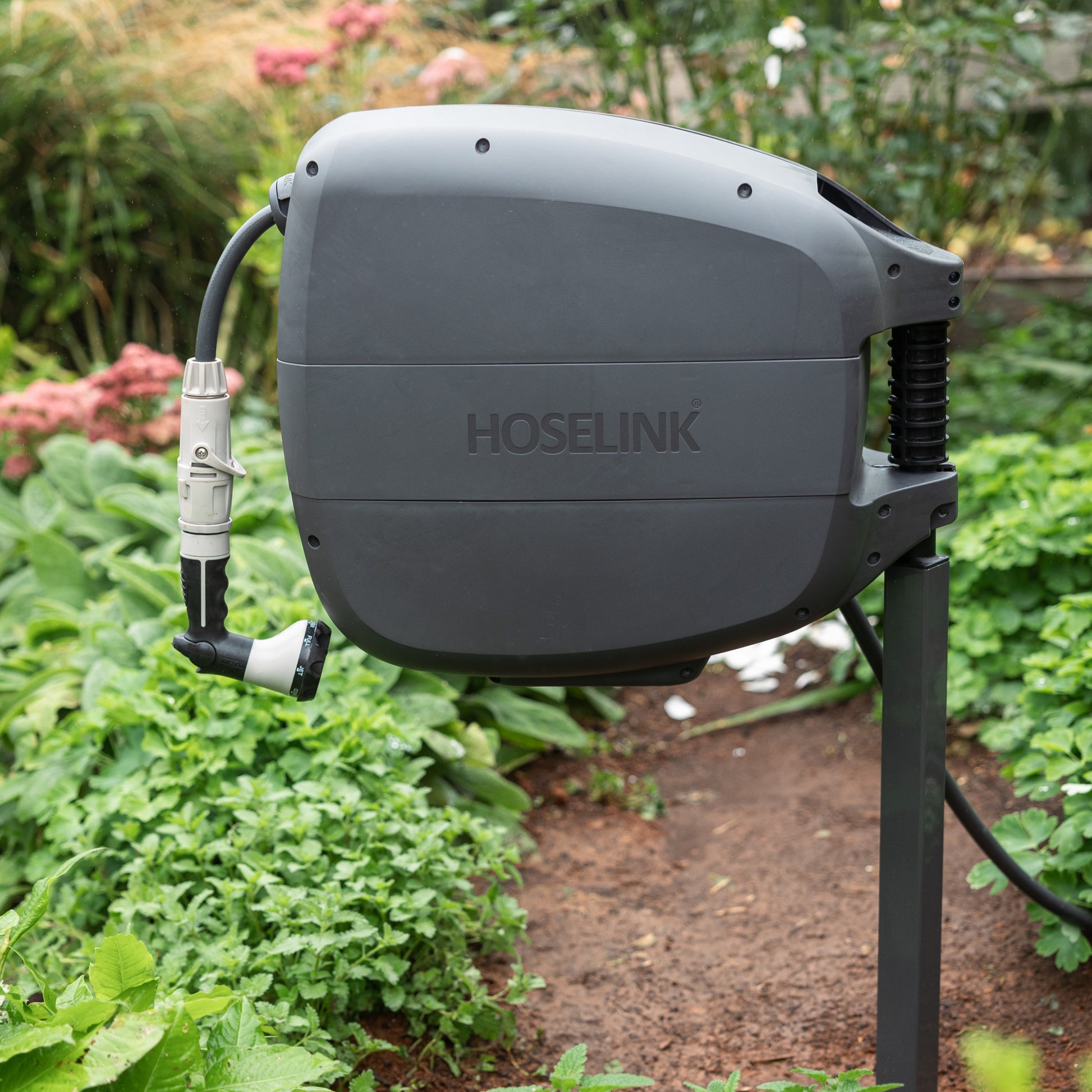 Charcoal Evolve Retractable hose Reel mounted on an Evolve Series mounting post in a garden surrounded by lush green foliage 