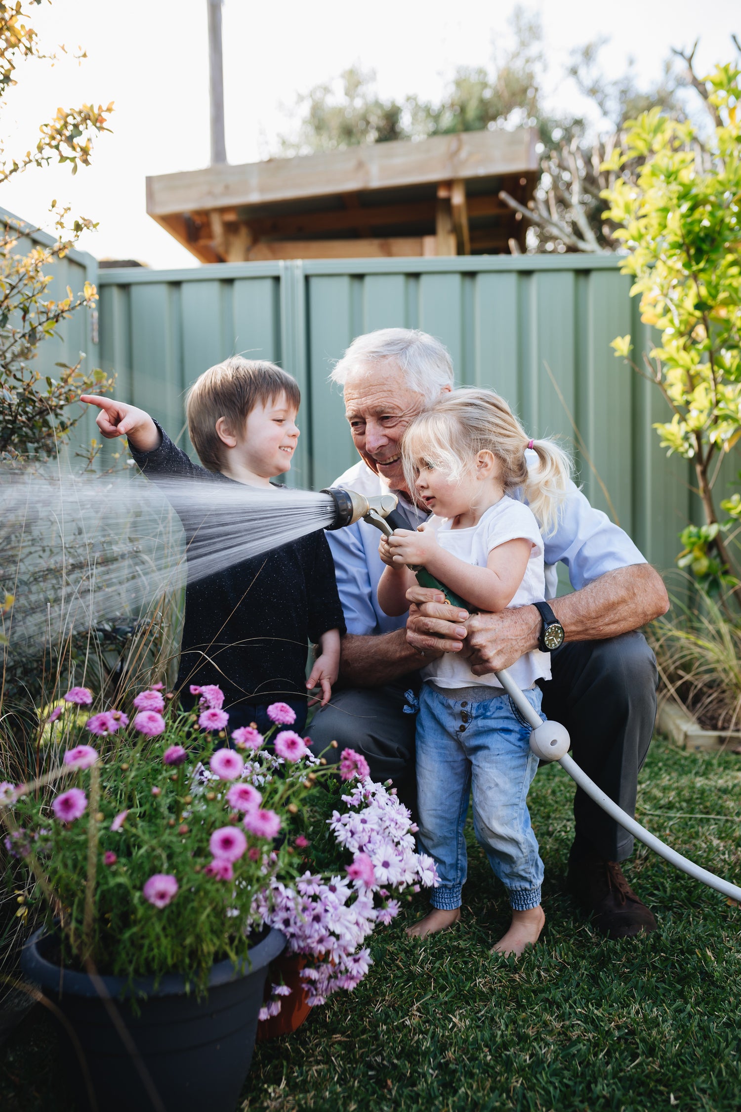 Granddad watering flowers in the garden with his grandson and grand daughter