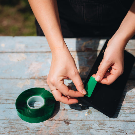 Double sided tape being applied to the back of a solar light on wooded table