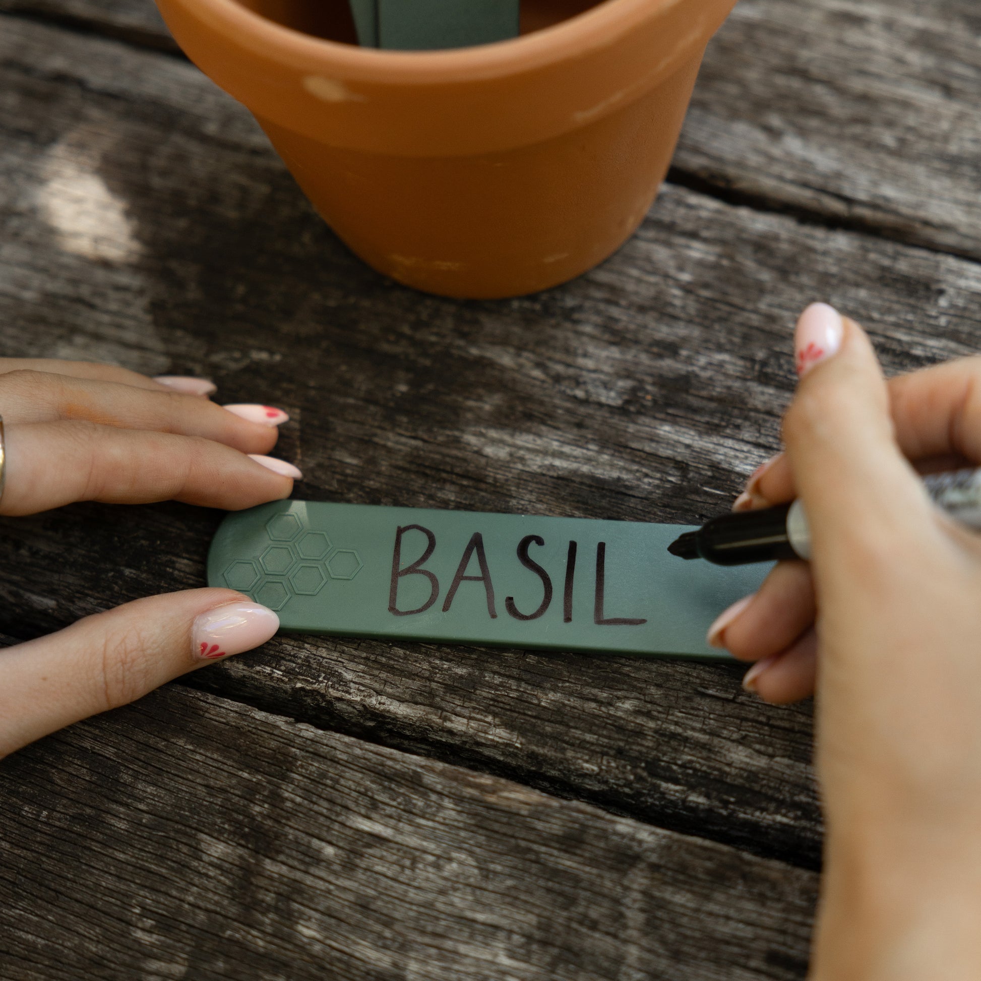 Person writing basil on a recycled plastic plant label on a garden bench
