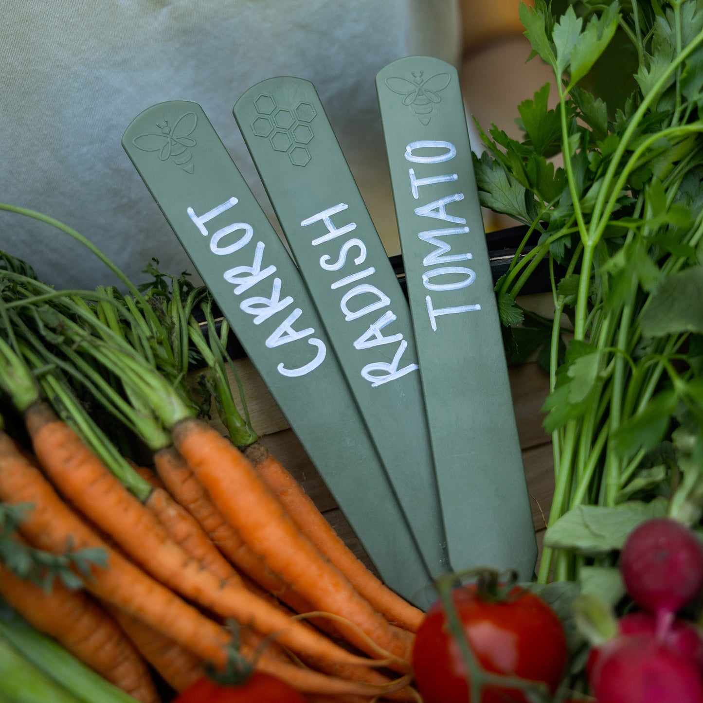 Set of three recycled plastic sage green plant labels in a basket of vegetables