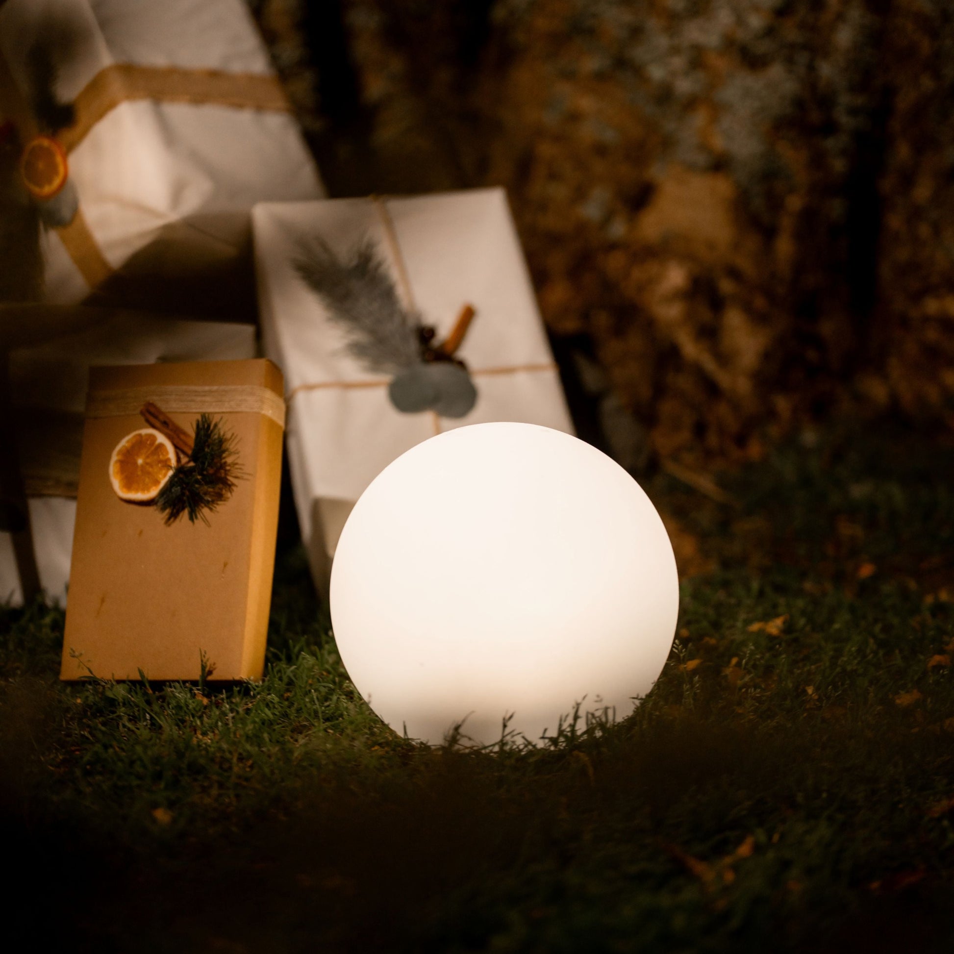 Glowing white sphere light on grass with wrapped presents and a book in the background