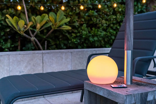 Outdoor setting with a solar sphere light on a table, surrounded by greenery and a lounge chair.