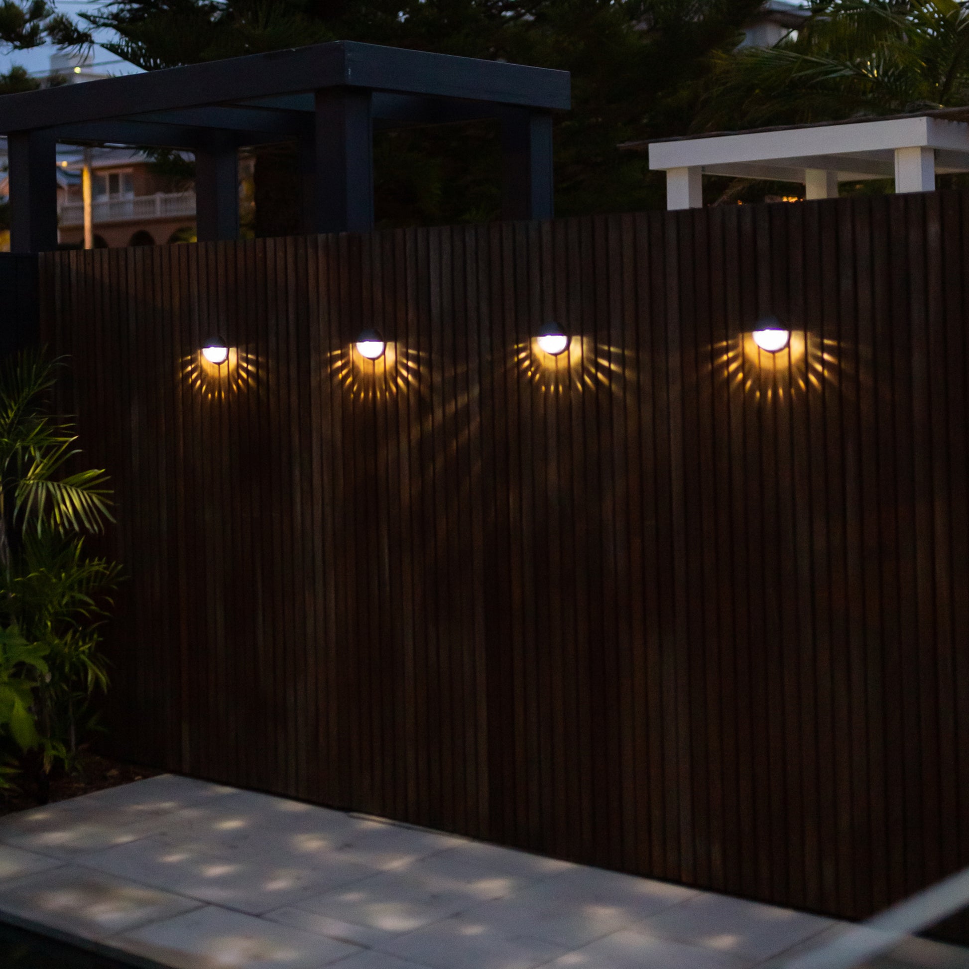 four round solar lights installed on a wooden wall with the lights showing a sun beam pattern beneath them