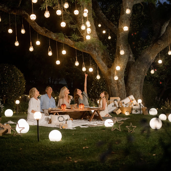 People enjoying a picnic under a tree with hanging lights and solar sphere lights at night.