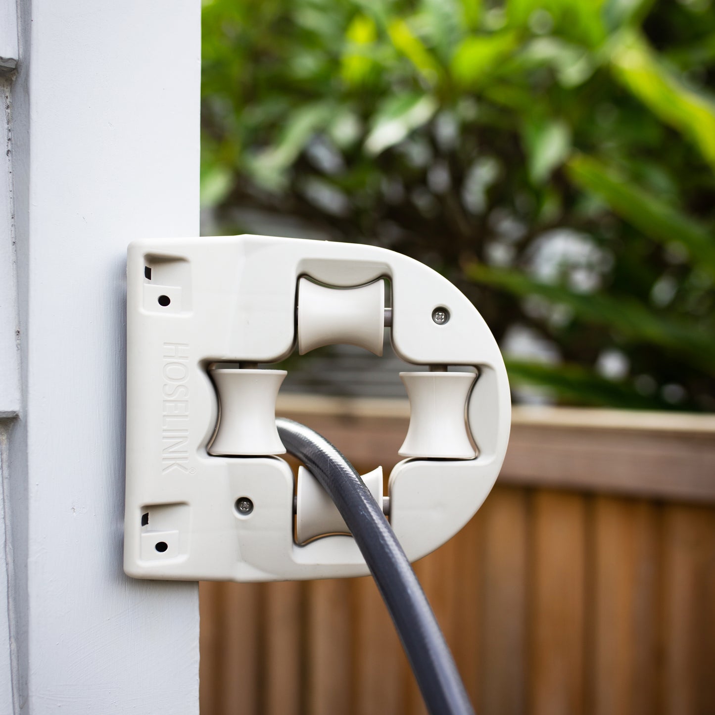 Close up image of a wall mount hose guide on a white wall with a hose going through it.