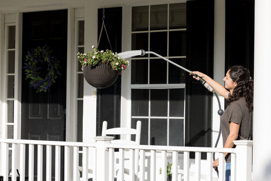 woman-holding-a-long-reach-shower-wand-watering-a-hanging-basket-of-flowers