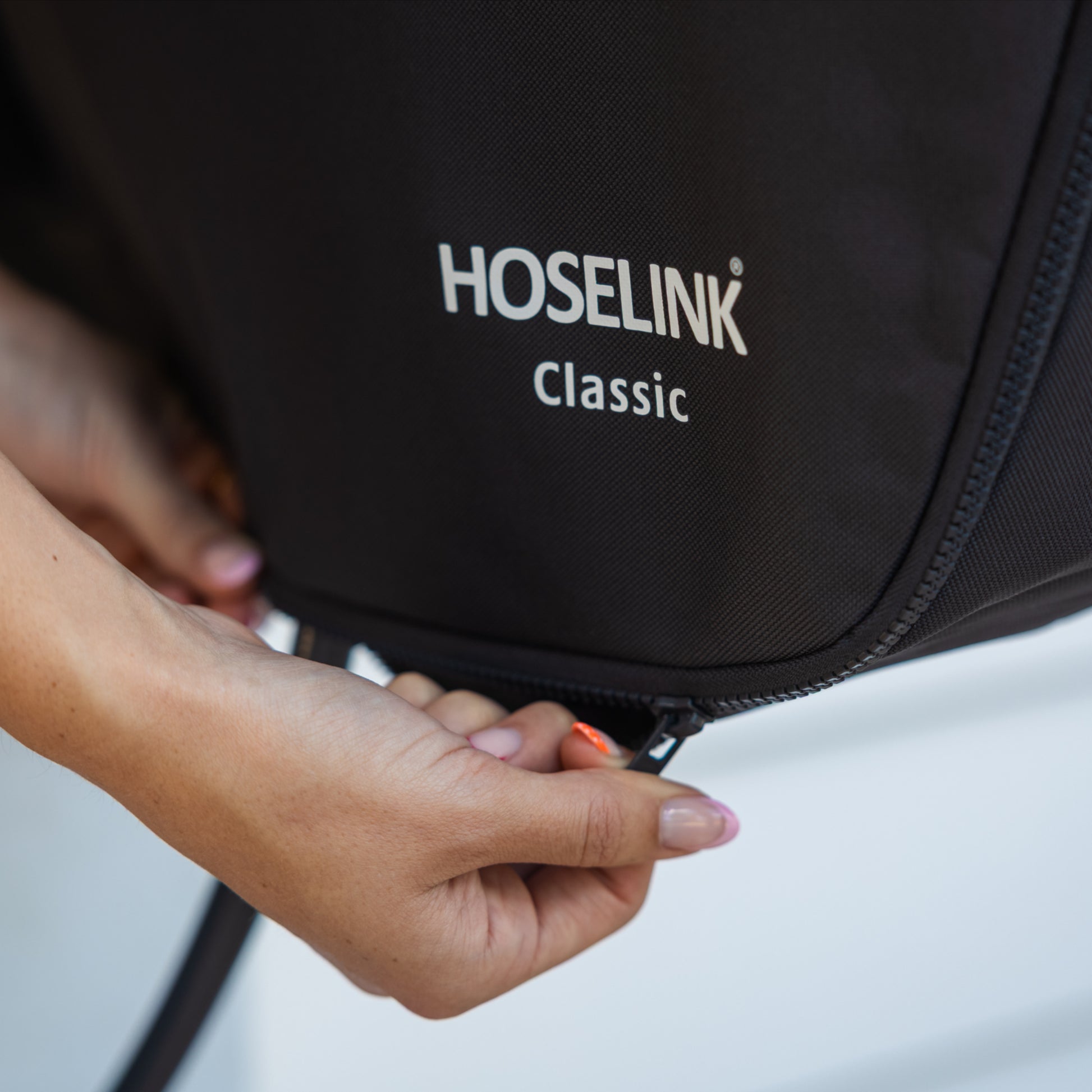 Close-up of a persson doing up the zipper on a charcoal classic hose reel cover below white logo