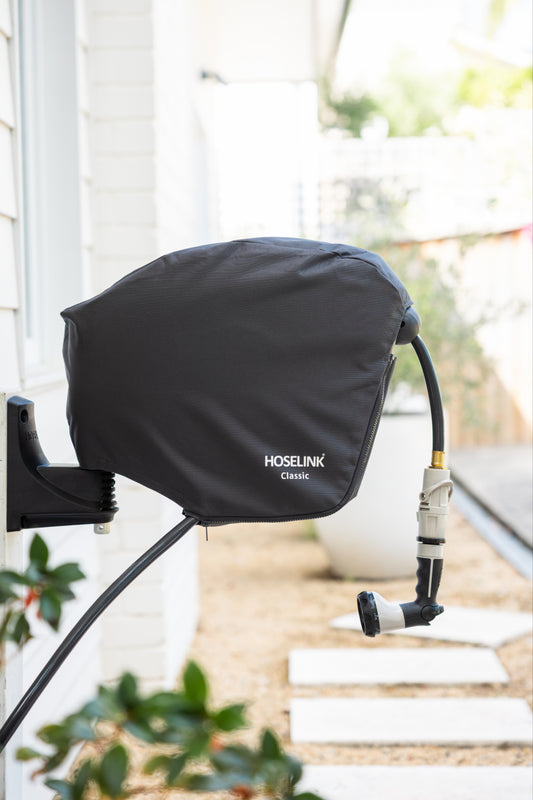 Charcoal Hoselink garden hose reel with cover attached to a wall with plants and steps in the background.