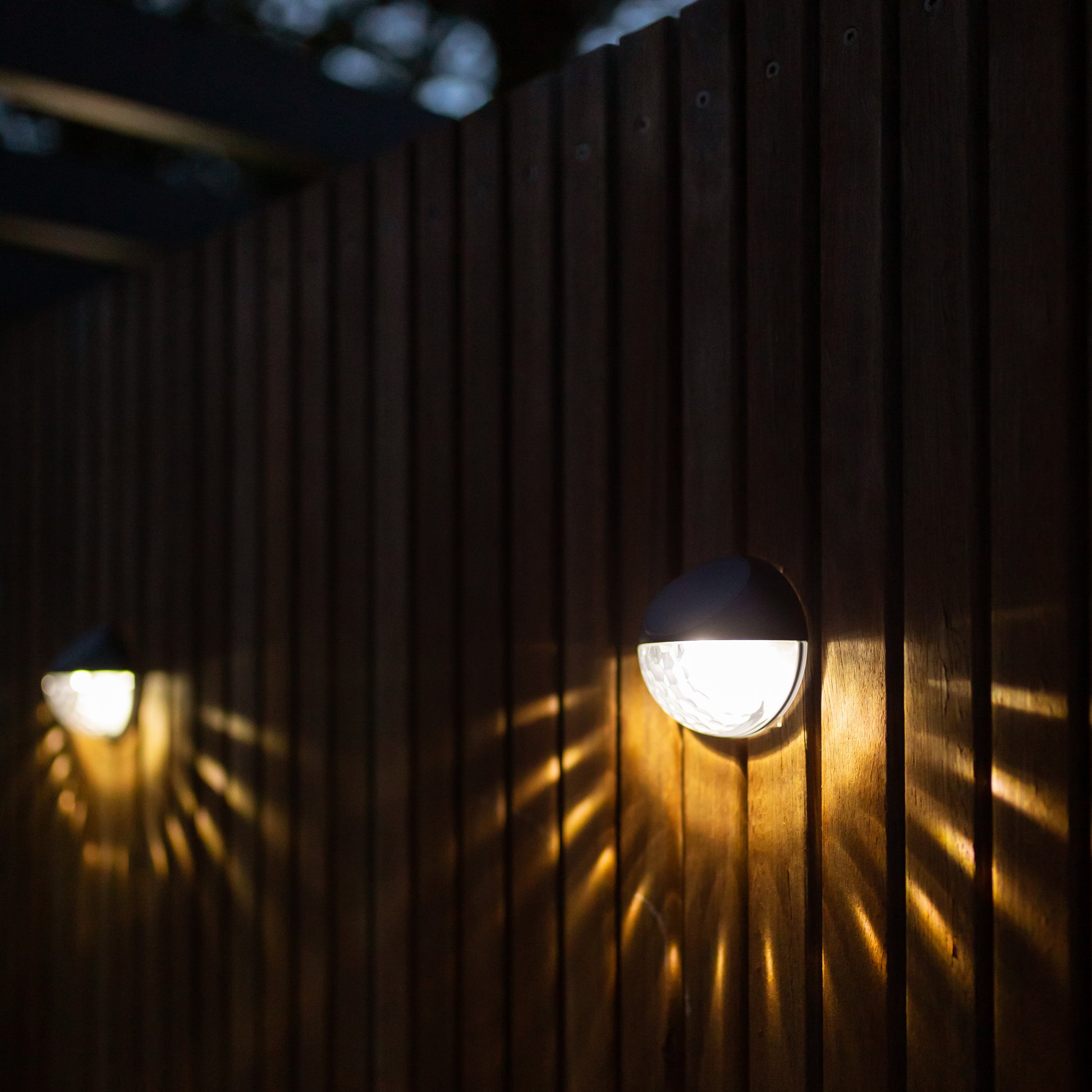 two round solar lights installed on a wooden beamed wall with light creating a sun pattern on wall on the lower half of the light