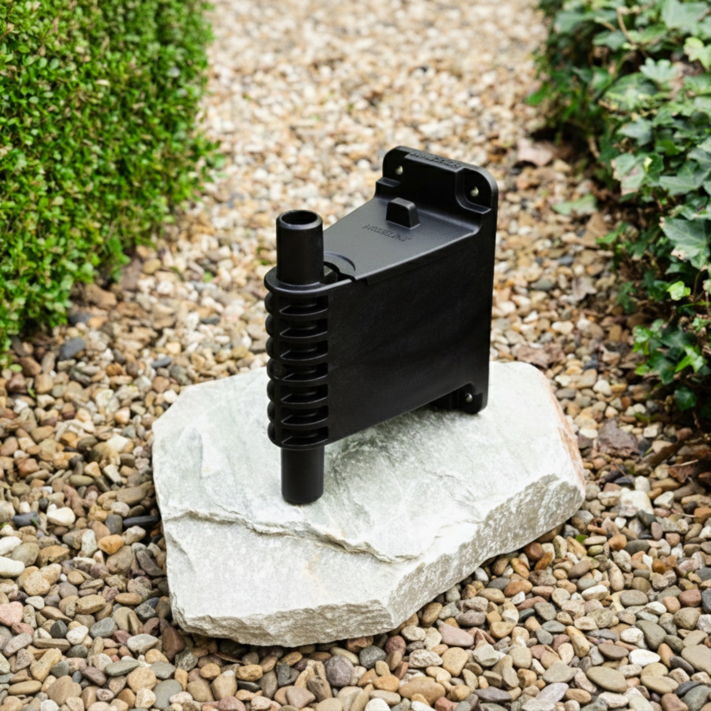 evolve wall bracket and lid sitting on a white stone on a gravel path between two green hedges