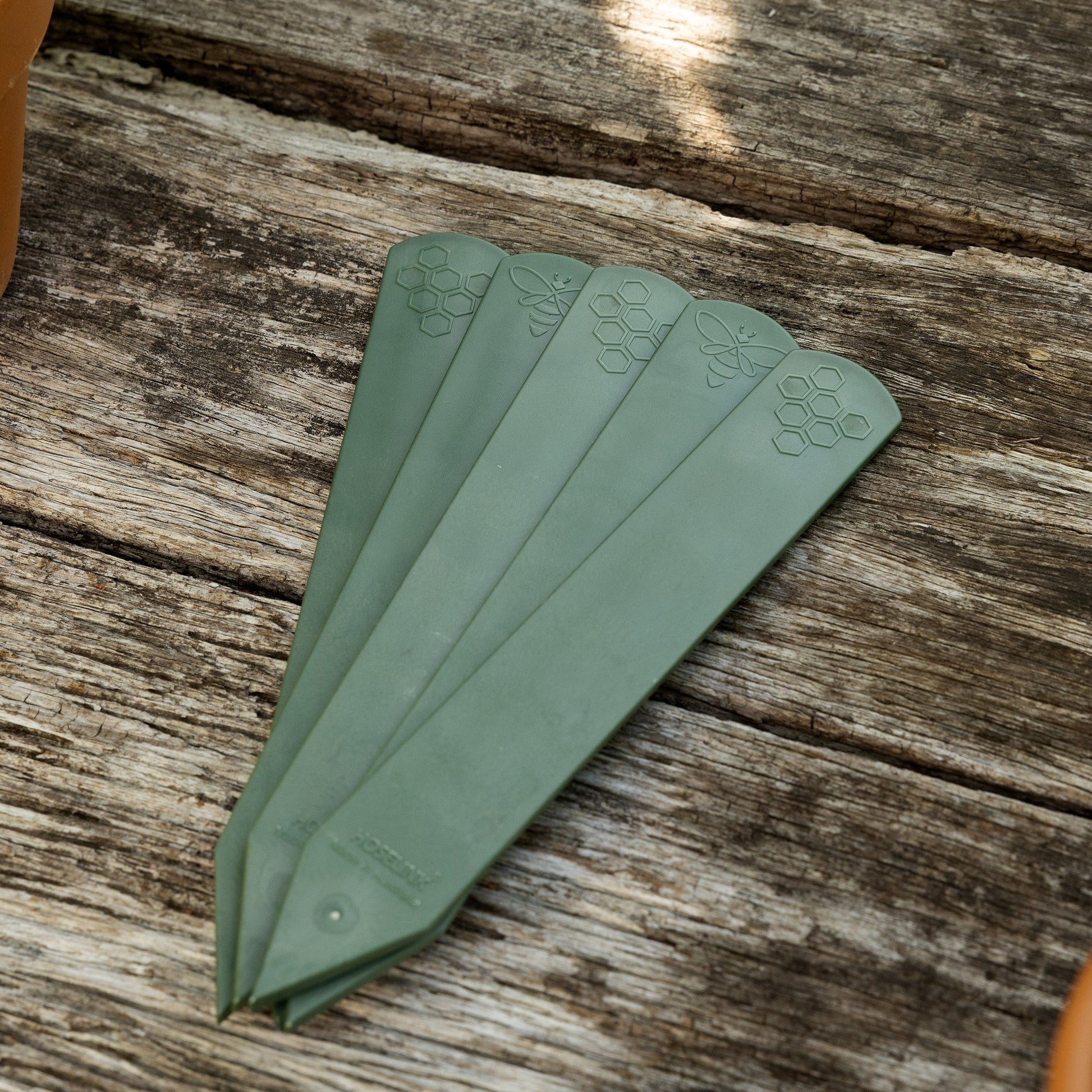 Set of five sage green recycled plastic plant labels on a wooden garden bench