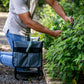 Person in grey shirt kneeling on Garden kneeler and seat trimming plants next to garden bed. 