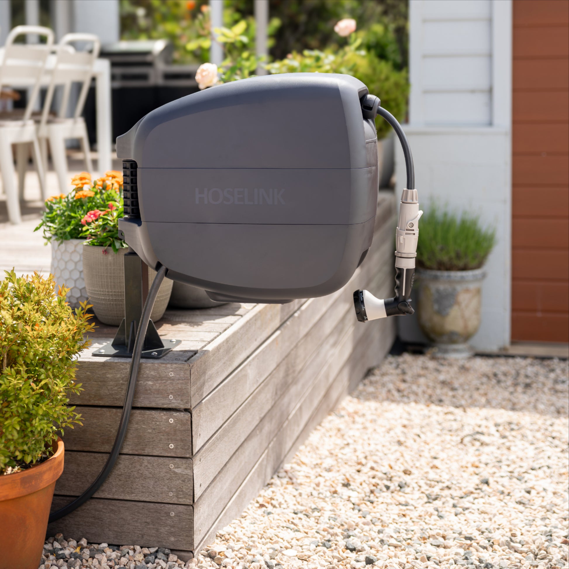 Evolve hose reel mounted on a wooden deck with plants and a house in the background.
