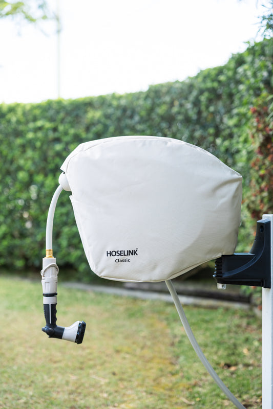 Beige classic hose reel cover isntalled on a Hoselink hose reel in a backyard with green lawn and hedges in the background