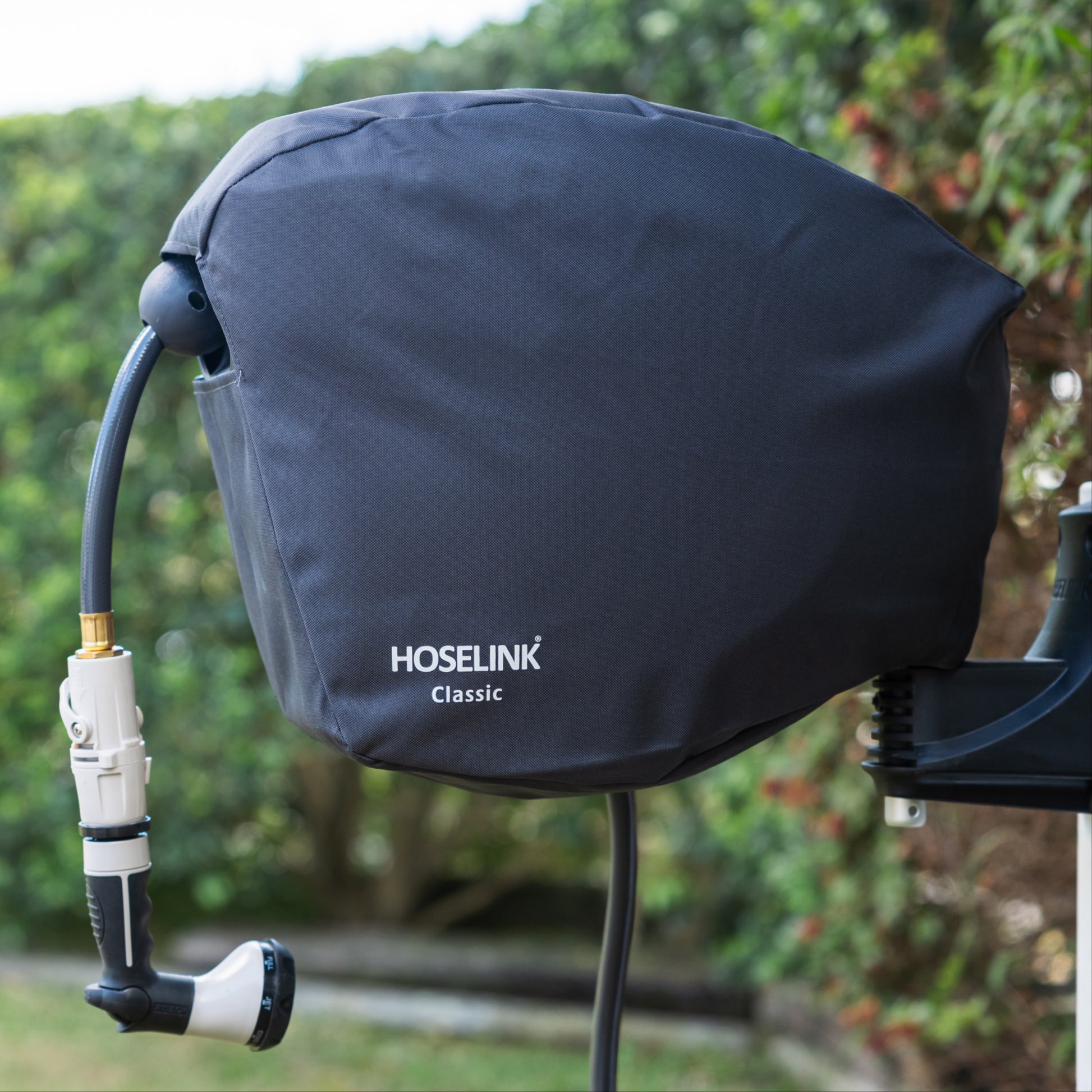 Charcoal HOSELINK Classic outdoor hose reel cover with hose attached to a white post with green lawn and hedges in the background 