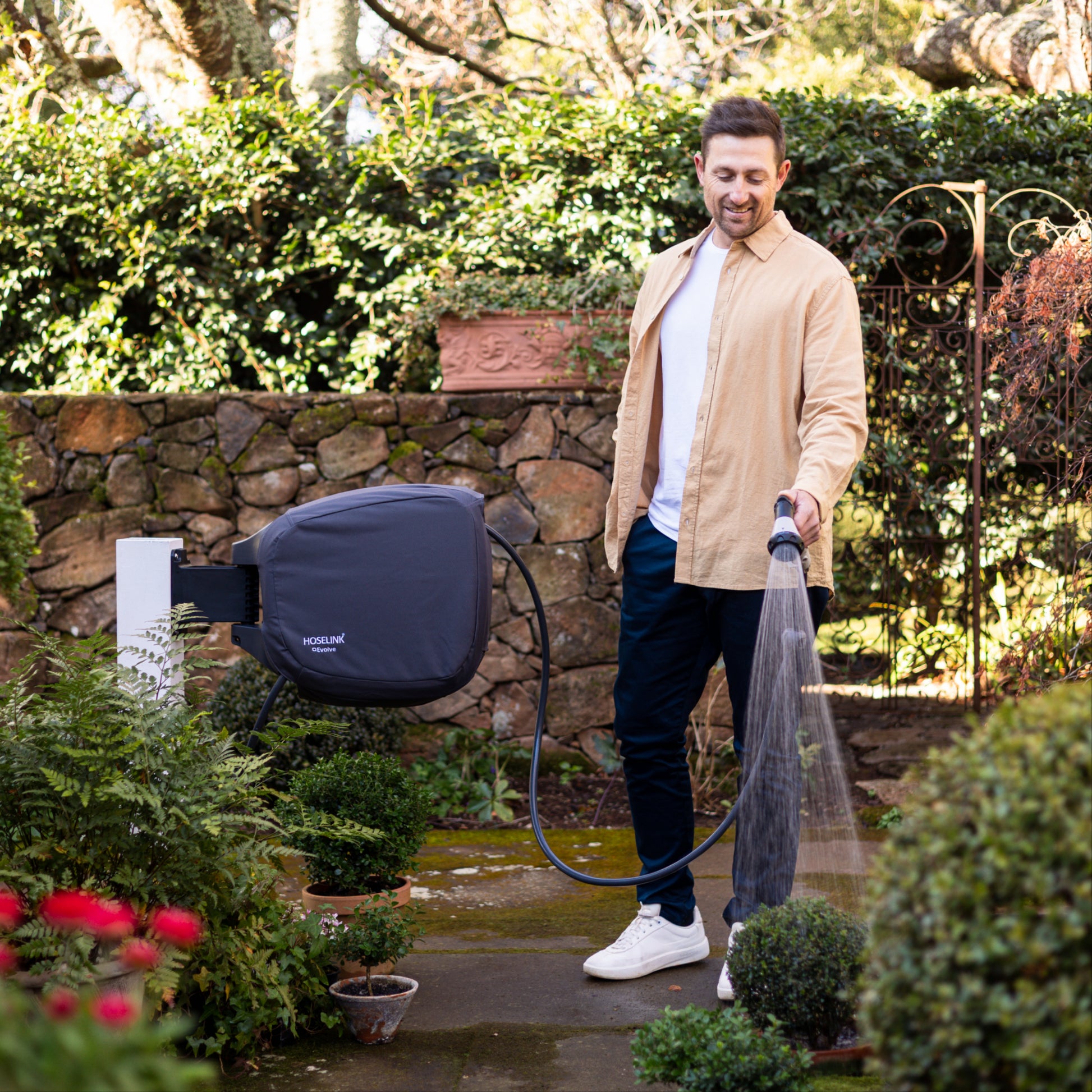 Man watering plants with an evolve hose reel in a charcoal cover in a garden setting with a stone wall in the background