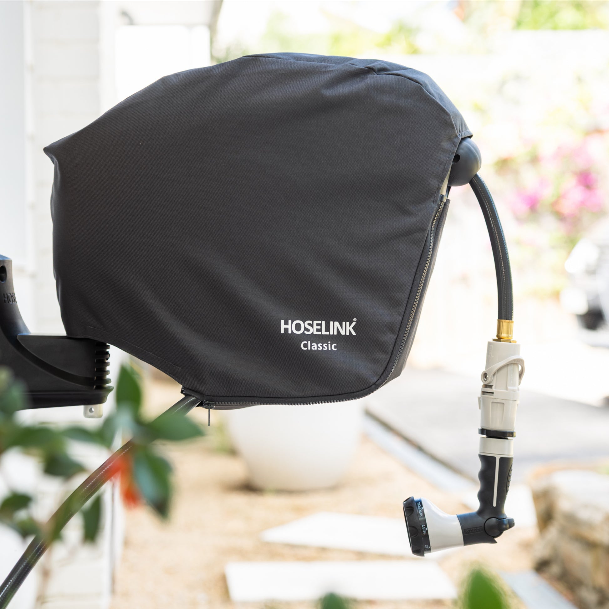 Charcoal Hoselink hose reel cover with white logo fitted to reel attached to a wall with plants and steps in the background.
