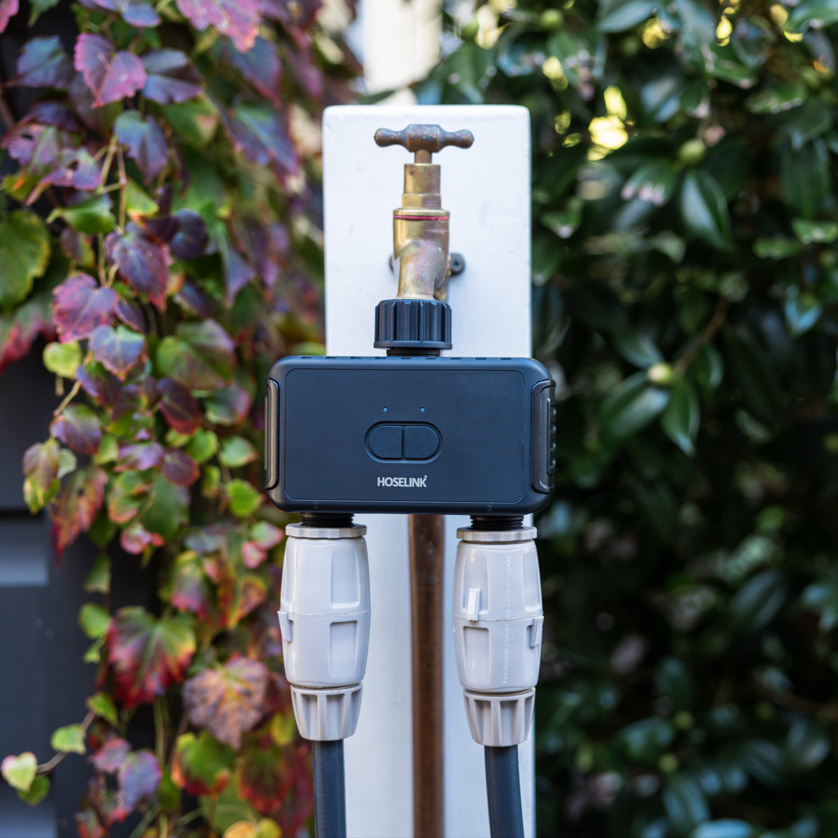 smart hose time dul outlet installed on an outdoor faucet on a white post with two hoses attahced